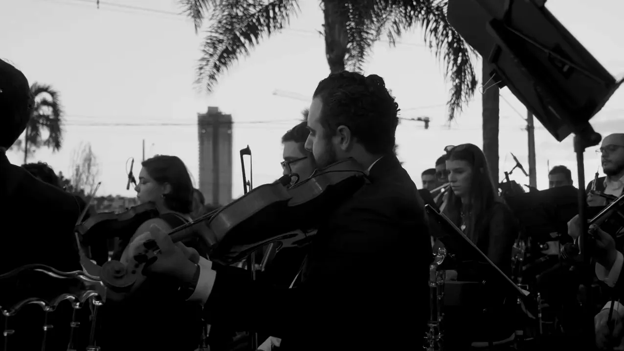 Naipe de cordas da Filarmônica Aruna tocando ao ar livre, ao pôr do sol, na estreia pública em Maringá