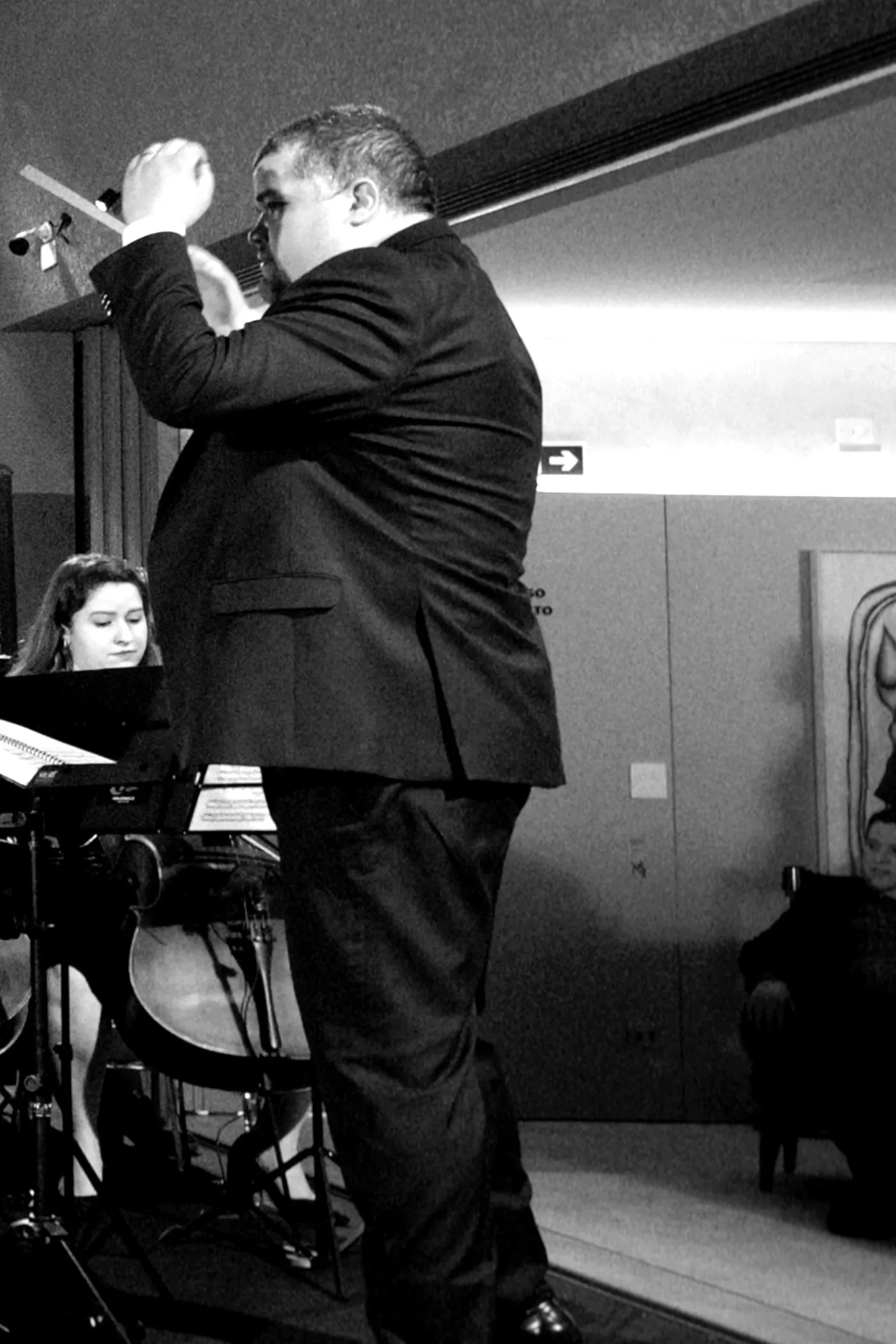 Maestro da Filarmônica Aruna regendo, batuta erguida, visto de lado