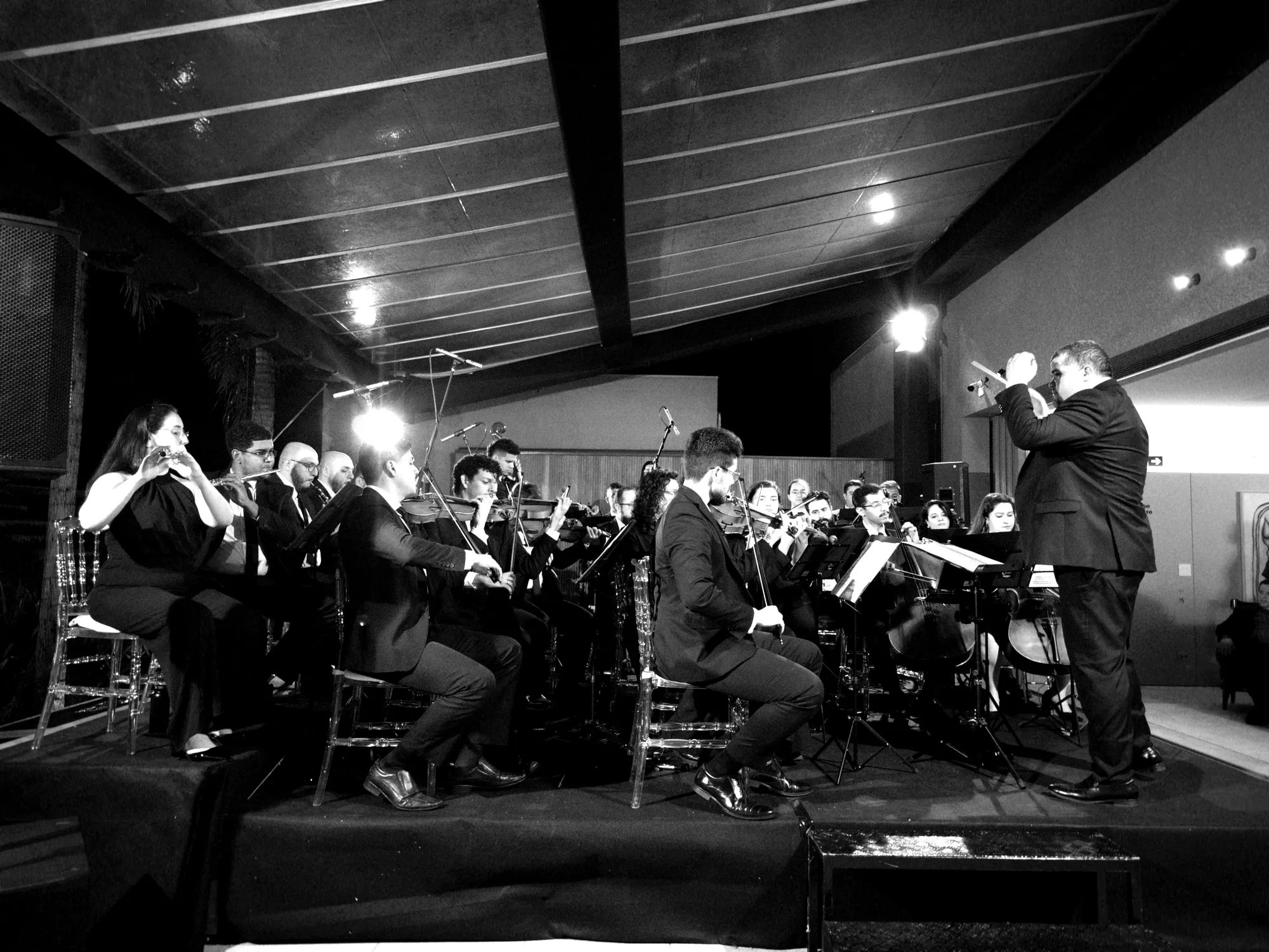 Filarmônica Aruna completa em apresentação no palco, maestro regendo à direita